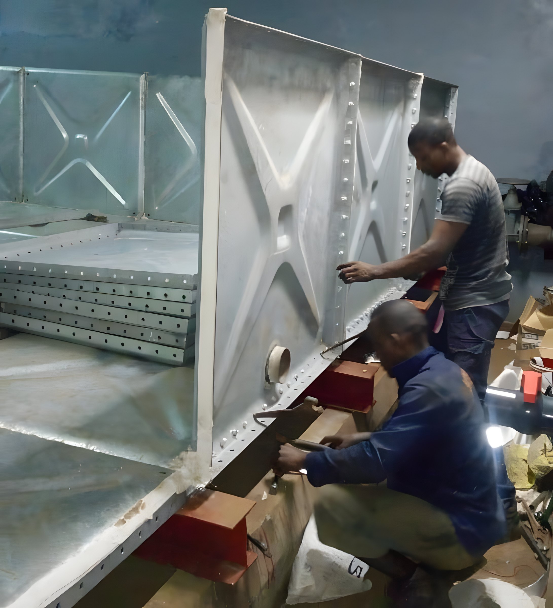 Installers bolting galvanised panels together to build a pressed steel tank